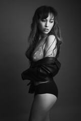 Fototapeta premium Black and white studio portrait of a beautiful woman in her 30s wearing black underwear, floral bra and a black leather jacket. Her hair is long dark and wet. She is looking to her side. 