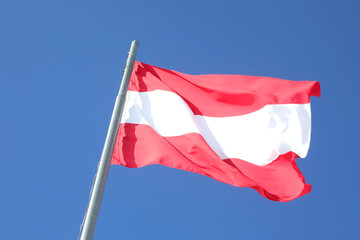 Large Austrian flag in white and red colors waving against a cloudless blue sky