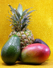 Tropical fruits paradise with pineapple avocado and mango on golden background for healthy eating and wellness concept