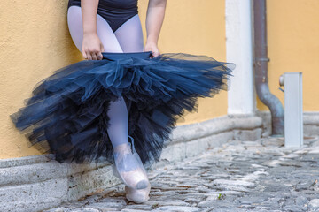Close up young female ballerina dressing up and putting on black tutu leaning on the yellow...