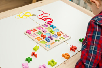 kid learning numbers through game. Sensory activity with wooden numbers and shoe laces. Educations at home, pre-school education, Montessori methodology. sequence of numbers, arithmetic problems.