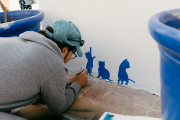 Caucasian adult man painting decorative three little cats on a tourist house building