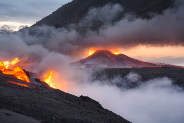 Dramatic fiery sunset paints the volcano's peak red as smoke billows from the fiery maw