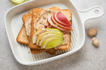 Toasts with peanut butter and fresh pear slices on a light-beige serving tray, horizontal shot, selective focus