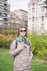 Beautiful stylish woman with sunglasses eats ice cream standing in the city park of Belgrade, Serbia