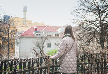 Beautiful woman standing back near iron fence and looking at buildings