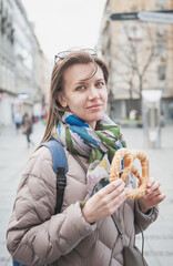 Beautiful young woman holds bagel outdoor on the street