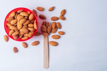 Almond nuts in a red bowl and wooden spoon on white background.