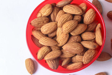 Close up of almonds in a red bowl on a white background.