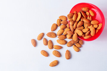 Top view of Almonds falling from a red bowl on a white background.
