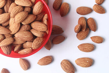 Almonds in a red bowl on a white background and scattered around it. closeup