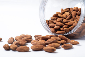 Almonds falling from a glass container leaning against a white background