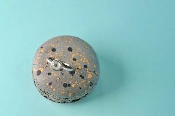 close-up of an engagement silver ring with a gemstone inserted in a grey speckled macaroni cake on an azure background