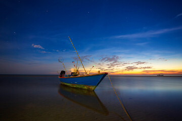 A small fishing boat on a beach in eastern Thailand with a beautiful sky and stars in nature at night.