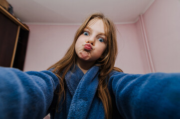 A smiling girl, a cheerful child teenager photographs herself with a camera, smartphone, phone...