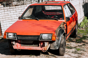 Red old abandoned broken rusty damaged retro car made in the USSR without a bumper after an...