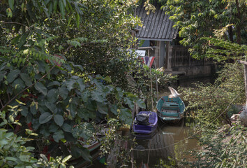Wooden rowboat and Small motor boat moored behind house on canal amongst trees and water. Space for...