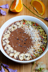 Chocolate smoothie bowl, made from raw cacao and banana and oat milk topped with cacao nibs, toasted shredded coconut, goji berry and match granola, chia and flax seeds 