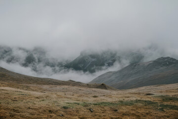 Fototapeta premium Steaming geothermal features peek through clouds in a mountainous landscape, creating a mystical scene reminiscent of Yellowstone National Park