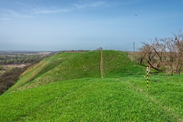 a path along a hill overgrown with green grass on the site of an ancient citadel surrounded by a moat near a village in the vicinity of the city of Ust-Labinsk (South Russia) on a sunny spring day