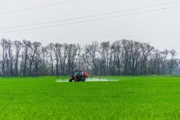 a tractor with a suspended container and an installation for spraying chemicals treats a field of winter wheat from pests and plant diseases near the Dvubratsky farm, southern Russia on a non-sunny da