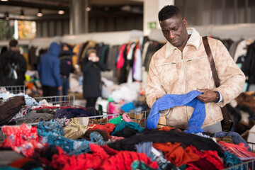 Ordinary Afro American guy considers things hands on flea market. High quality photo