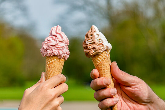Hands holding melting ice cream waffle cone in hands on summer light nature background