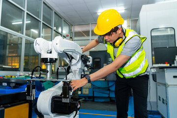 Manufacturing industry factory manufacturing technology concept. Professional male technician engineer in safety wear checking robotic machine arm system in production line for repair and maintenance.