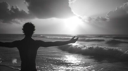 A man stands with his arms outstretched on the beach sunset, silhouette style, monotone black-white - obrazy, fototapety, plakaty