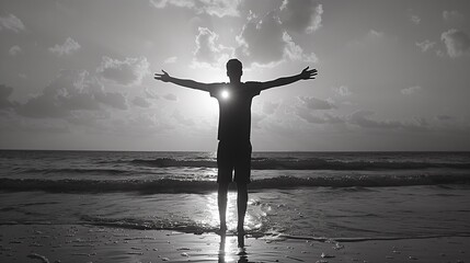 A man stands with his arms outstretched on the beach sunset, silhouette style, monotone black-white - obrazy, fototapety, plakaty
