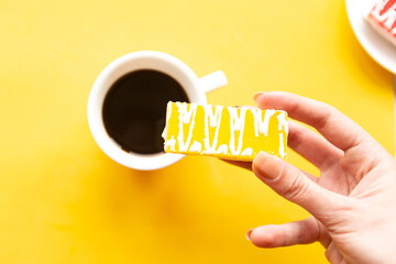Woman 's hand holds a cake over bright yellow background, minimal concept