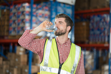 Warehouse male worker drinking water in break time in warehouse storage. Male worker drinking water...