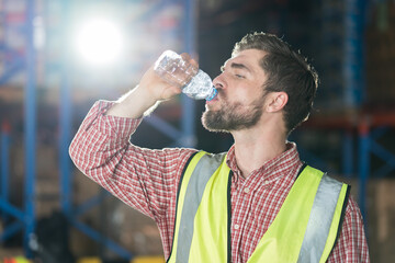Warehouse male worker drinking water in break time in warehouse storage. Male worker drinking water...