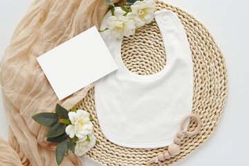 Template for pregnancy or baby waiting announcement, white baby bib and card mockup for ultrasound photo presentation, aesthetic floral flat lay.