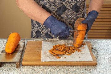 Woman peels fresh carrots with a knife over a kitchen board indoors. Close-up