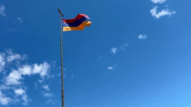 Armenian flag with flagpole waving in wind, rolling clouds and blue sky background 
