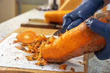 Cook peels fresh carrots with a knife over a kitchen board. Close-up. homemade food