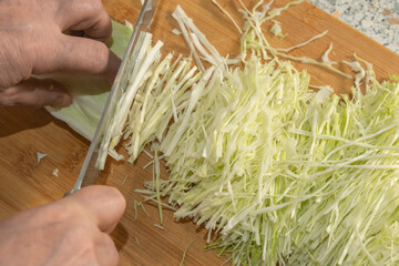 A Cook thinly slices white cabbage with a knife on a wooden cutting board to prepare a vegetable salad. Close-up. Veganism and raw food diet concept.