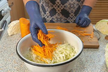 Woman adds thinly sliced carrots to shredded cabbage to ferment or make a salad. Healthy eating