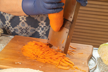 The cook grates carrots on a homemade wooden grater for making salad or fermenting. Healthy eating