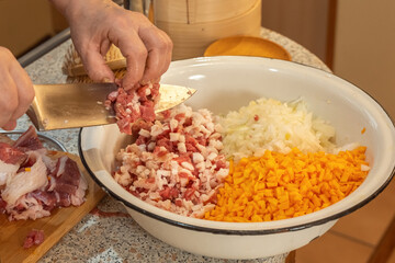 Cook pours finely chopped meat from a knife into a bowl with chopped onions and pumpkin to prepare minced meat.