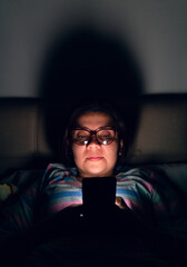 Latin woman from the front with a serious expression looking at her cell phone lying in her bed at...