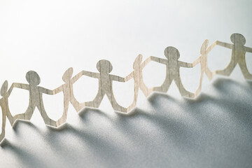 Paper human chain holding hands together and standing against the bright light, strong teamwork concept