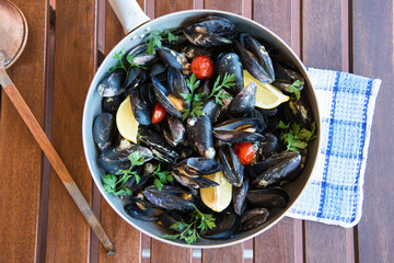 Moscioli or Cozze del Conero Ancona cooked in a pan with cherry tomatoes, garlic, parsley and chilli pepper on wooden background