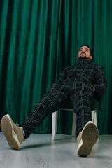 A man in a tracksuit sits on a chair on a green background