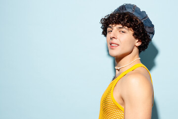 Side profile view close up young happy gay Latin man wear mesh tank top hat clothes look camera isolated on plain pastel light blue background studio portrait Pride day June month love LGBT concept.