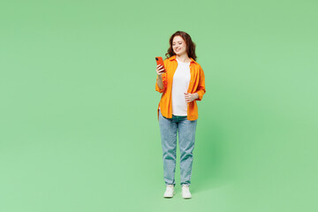 Full body young ginger fun woman she wear orange shirt white t-shirt casual clothes hold in hand use mobile cell phone chat online isolated on plain pastel light green background. Lifestyle concept.
