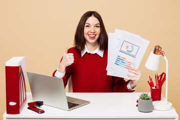 Young employee business woman wear red sweater shirt sit work at office desk with pc laptop hold...