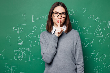 Young smart teacher woman she wear grey casual shirt glasses say hush be quiet finger on lips shhh...
