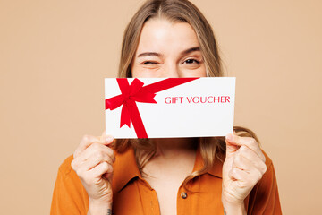 Young woman she wear orange shirt casual clothes hold cover mouth with gift certificate coupon voucher card for store isolated on plain pastel light beige background studio portrait Lifestyle concept